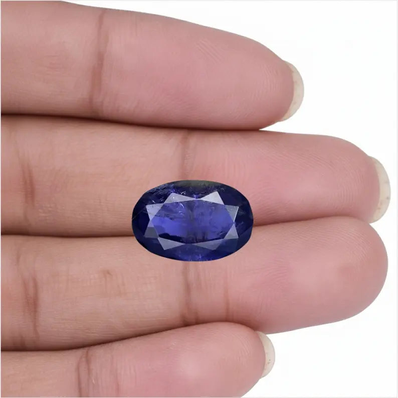 Natural oval facet cut Blue Iolite Neeli stone held in fingers showing deep blue color - Tathastu Gems