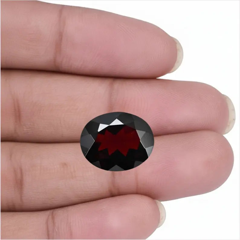 Natural oval cut Red Garnet gemstone held in fingers showing authentic deep red color and clarity - Tathastu Gems